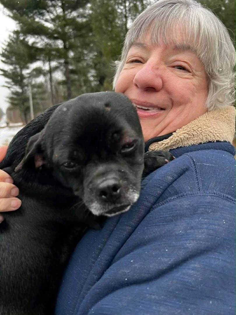 Woman cuddling a small black dog outdoors in winter